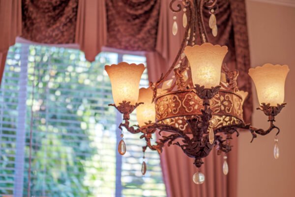 Chandelier with ornate design and warm lighting, enhancing the elegant interior of a Windermere home, featuring large windows and luxurious drapery.