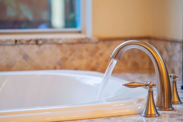 Elegant bathroom faucet pouring water into a luxurious white bathtub with marble countertop, showcasing upscale features in a custom home.