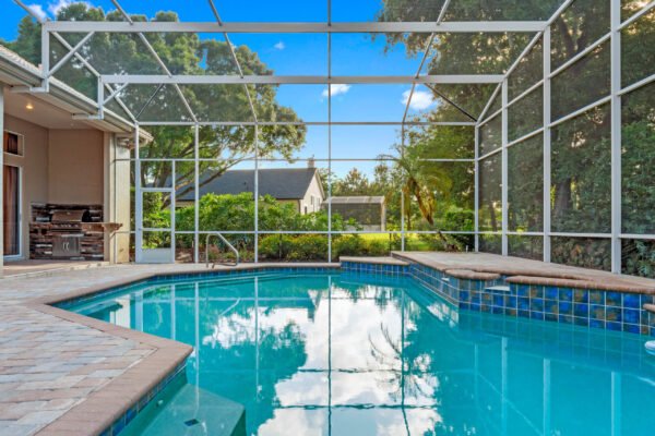 Screened-in pool area with a sparkling blue pool, surrounded by lush greenery and a patio featuring pavers, showcasing outdoor living space in Windermere, Florida.