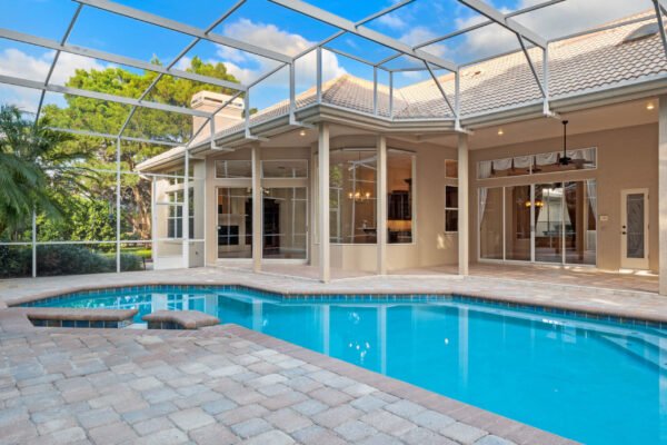Custom home pool area with screened enclosure, paver patio, and large windows overlooking lush greenery in Windermere, Florida.