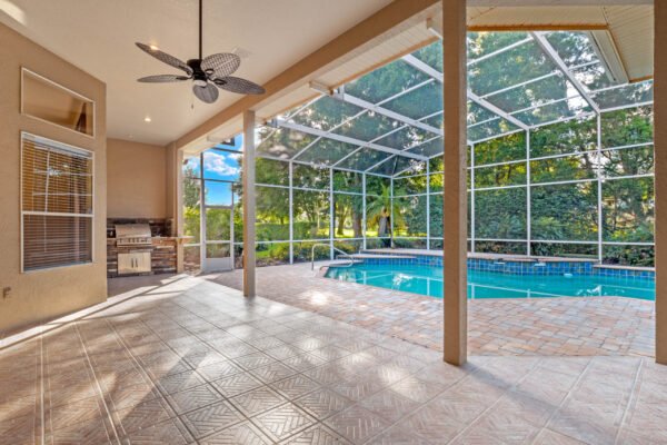 Screened-in lanai featuring a swimming pool, outdoor kitchen area, and spacious tiled flooring, surrounded by lush greenery in Windermere, Florida.