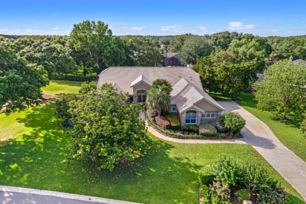 Aerial view of a stunning custom home at 11359 Willow Gardens Drive in Windermere, Florida, surrounded by lush landscaping and mature trees, highlighting the spacious over 1/2 acre lot and inviting curb appeal.
