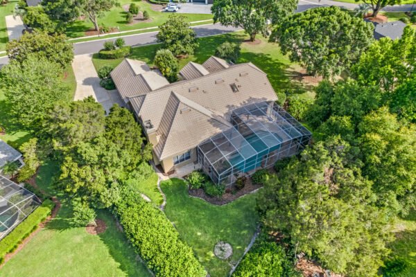 Aerial view of a custom home on over 1/2 acre lot in Windermere, Florida, featuring a screened-in pool area, lush landscaping, and a spacious yard surrounded by trees.