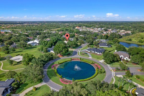 Aerial view of Willow Gardens Drive in Windermere, Florida, showcasing a tranquil residential community with a central pond, landscaped gardens, and nearby homes, emphasizing the serene environment and proximity to nature.