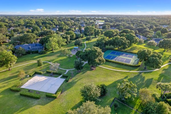 Aerial view of a community park in Windermere, Florida, featuring tennis courts, walking paths, and lush greenery, showcasing outdoor recreational amenities near 11359 Willow Gardens Drive.