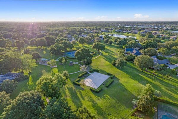 Aerial view of expansive green landscape in Windermere, Florida, showcasing manicured lawns, trees, walking paths, and nearby residential homes, emphasizing the tranquil community setting near 11359 Willow Gardens Drive.