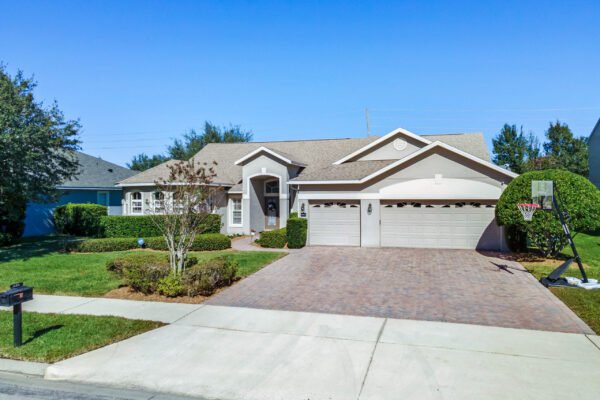 Single-story home at 13915 Zephermoor Lane in Winter Garden, Florida, featuring a brick driveway, three-car garage, manicured landscaping, and a basketball hoop in the front yard.