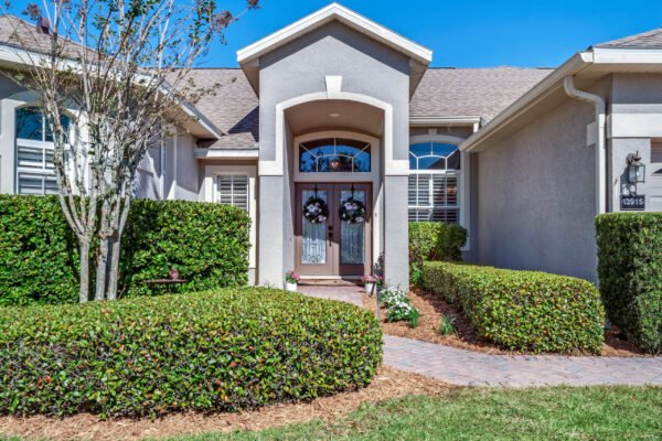 Front entrance of 13915 Zephermoor Lane in Winter Garden, FL, featuring double entry doors, decorative wreaths, landscaped hedges, and a brick pathway, highlighting the home's curb appeal in a gated community.
