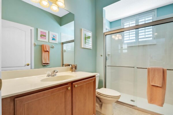 Bathroom with light blue walls, wooden cabinetry, and modern fixtures, featuring a glass shower, toilet, and decorative wall art, highlighting the home's stylish design at 13915 Zephermoor Lane, Winter Garden.