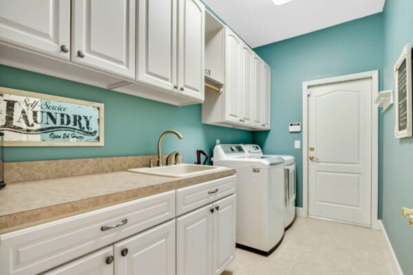 Laundry room with white cabinets, beige countertop, sink, and washer/dryer units, featuring teal walls and a "Laundry" sign, highlighting the home's functional space in 13915 Zephermoor Lane, Winter Garden, FL.