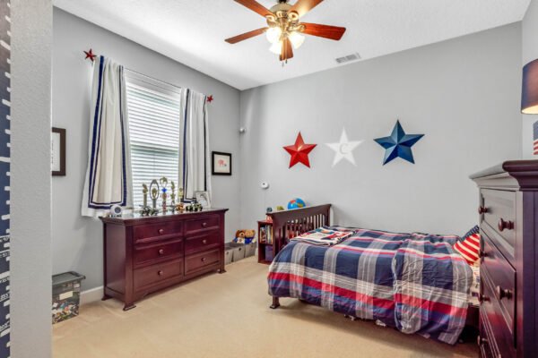 Bedroom featuring a twin bed with plaid bedding, wooden dresser, and star decorations on the wall, showcasing a cozy and playful space ideal for children.