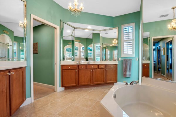 Spacious bathroom with green walls, double vanity, and large mirrors, featuring a soaking tub and decorative lighting, showcasing luxury in the Winter Garden home at 13915 Zephermoor Lane.