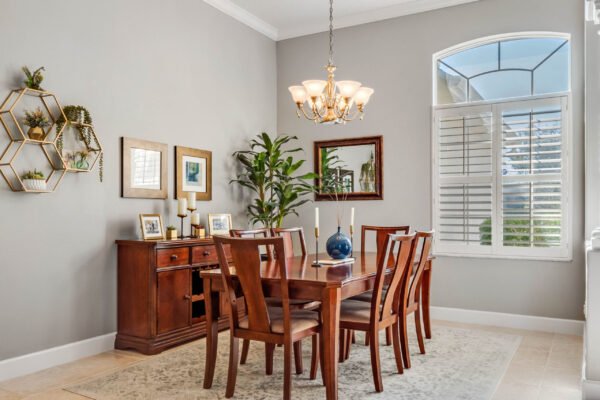 Dining area featuring a wooden table surrounded by chairs, elegant chandelier, decorative wall art, and a large window with plantation shutters, showcasing a bright and inviting atmosphere in a Winter Garden home.