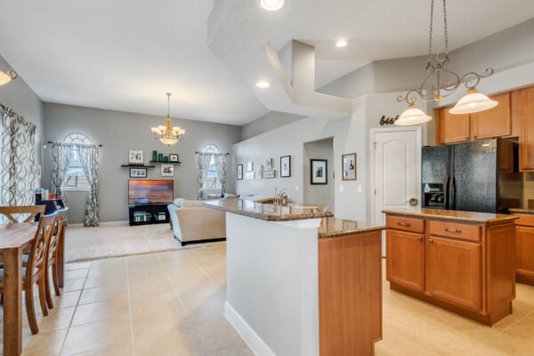 Modern kitchen and living area in Winter Garden home, featuring wooden cabinets, granite countertops, and dining space, showcasing open floor plan and natural light from large windows.