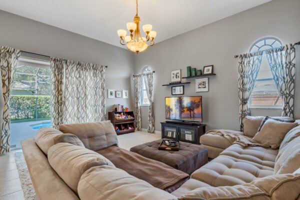 Cozy living room featuring a sectional sofa, chandelier, and large windows with pool views, showcasing a modern design suitable for family gatherings in a Winter Garden home.