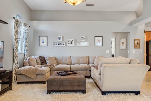 Cozy living room featuring a sectional sofa, decorative throw pillows, and a plush ottoman on a soft rug, with framed pictures on the wall, showcasing the inviting interior of the home at 13915 Zephermoor Lane, Winter Garden, FL.
