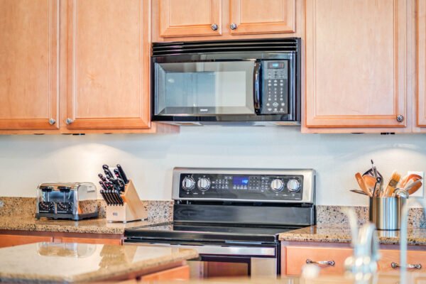 Modern kitchen with granite countertops, black stove and microwave, wooden cabinetry, and stainless steel appliances, showcasing a well-equipped cooking space.
