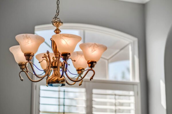 Chandelier with six frosted glass shades hanging in a well-lit room featuring large arched windows and plantation shutters, highlighting the elegant interior design of the home at 13915 Zephermoor Lane, Winter Garden.