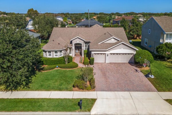 Aerial view of 13915 Zephermoor Lane, a single-story, four-bedroom, three-bathroom home in Winter Garden, Florida, featuring a brick driveway, landscaped front yard, and a three-car garage, set in a quiet neighborhood.