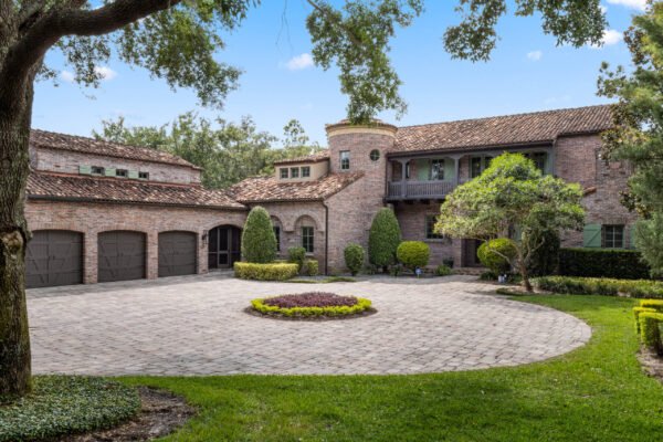 Luxury home exterior at 11019 Bridge House Road in Windermere, FL, featuring a brick façade, landscaped circular driveway, and lush greenery, highlighting its upscale design and lakefront location.