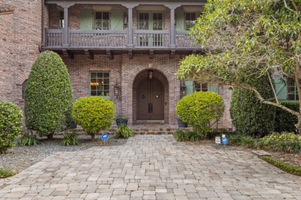 Luxury home entrance at 11019 Bridge House Road, Windermere, FL, featuring brick exterior, arched doorway, landscaped greenery, and stone paver driveway.