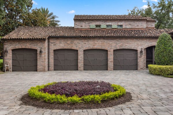 Luxury home garage with three dark wooden doors, brick exterior, and landscaped circular flower bed, located at 11019 Bridge House Road, Windermere, FL.