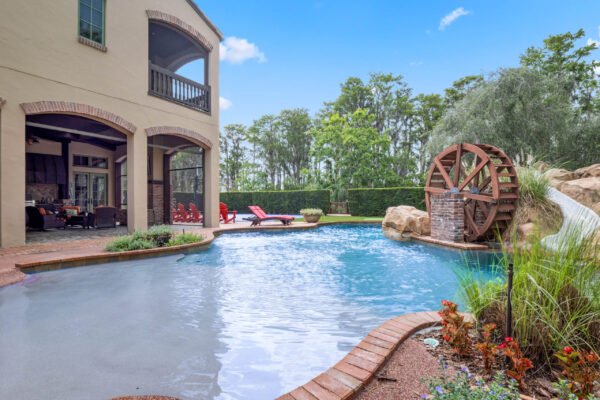 Luxury lakefront home in Windermere with a resort-style pool, featuring a water wheel, lush landscaping, and outdoor seating area, showcasing the Florida lifestyle.