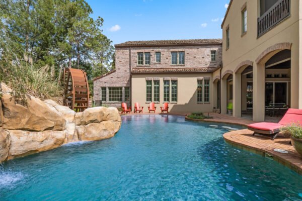 Luxury lakefront home at 11019 Bridge House Road, featuring a stunning pool with rock waterfall, surrounded by lush greenery and elegant outdoor seating, embodying the Florida lifestyle.