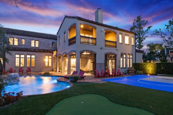 Luxury home exterior at dusk featuring a lakefront pool, covered lanai, and basketball court in Windermere, FL, highlighting outdoor living and entertaining spaces.