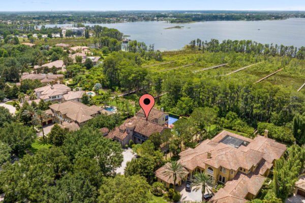 Aerial view of a luxury home at 11019 Bridge House Road in Windermere, FL, showcasing its expansive grounds, surrounding greenery, and proximity to a lake, with a location marker indicating the property's position.