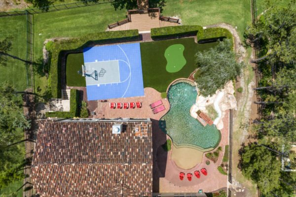Aerial view of luxury home at 11019 Bridge House Road, featuring a basketball court, putting green, and a resort-style pool with lounge chairs in Windermere, FL.