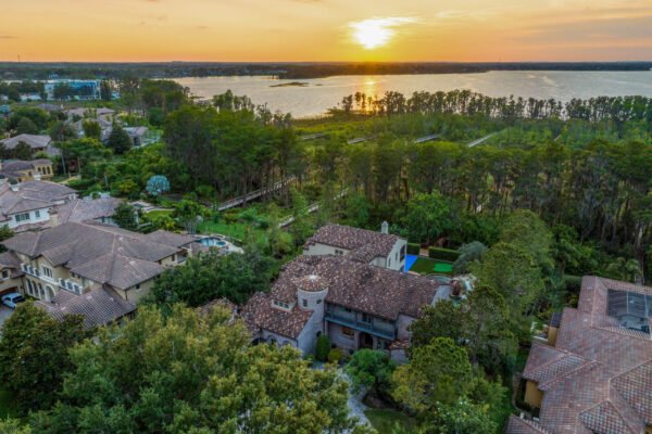 Aerial view of luxury home at 11019 Bridge House Road in Windermere, FL, showcasing expansive lakefront property, lush greenery, and sunset over Lake Butler.