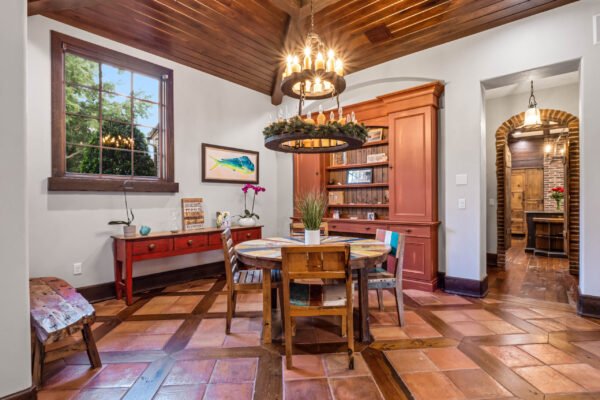 Elegant dining area featuring a round wooden table, colorful chairs, and a striking chandelier, complemented by a built-in bookshelf and large window, showcasing the luxurious interior design of the Windermere estate at 11019 Bridge House Road.