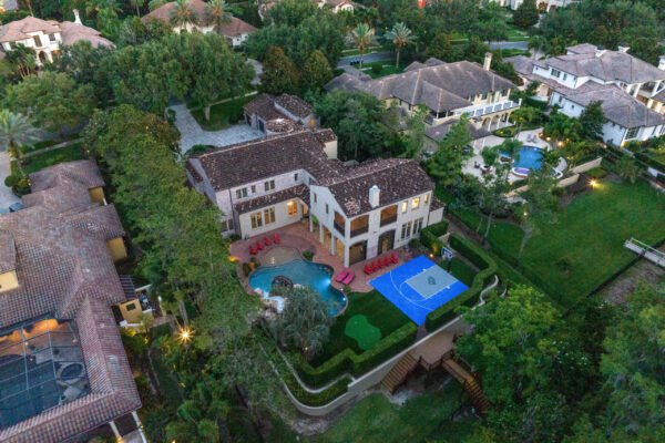 Luxury lakefront home at 11019 Bridge House Road, Windermere, FL, featuring a spacious pool area, outdoor seating, and a basketball court, surrounded by lush landscaping and upscale residences.