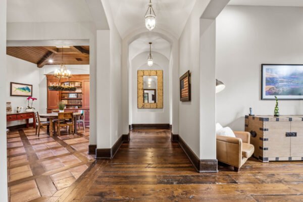 Luxurious interior hallway featuring arched ceilings, warm wooden flooring, decorative wall art, and a view into an elegant dining area with a chandelier, showcasing the custom design of the estate at 11019 Bridge House Road in Windermere, FL.
