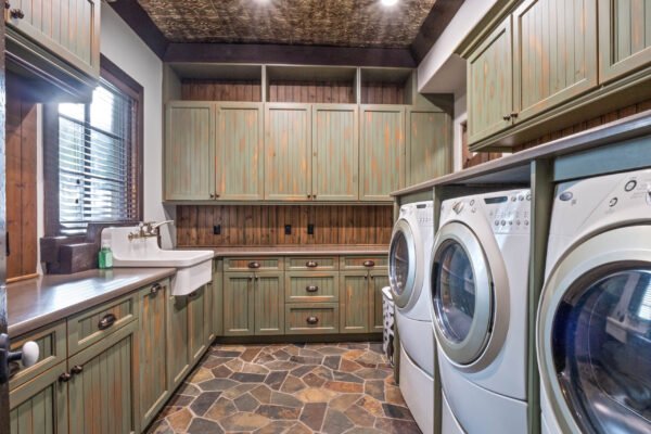 Laundry room featuring modern appliances, rustic cabinetry, stone flooring, and a utility sink, highlighting the luxury and functionality of the home at 11019 Bridge House Road, Windermere, FL.