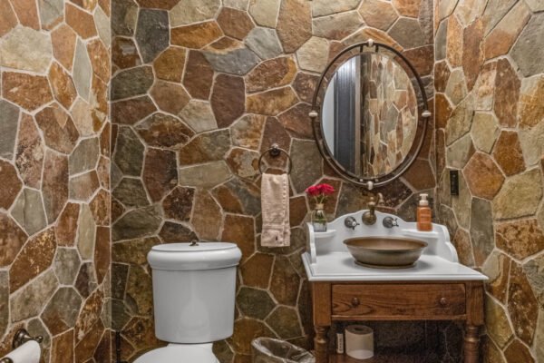 Luxurious bathroom featuring rustic stone walls, vintage wooden vanity with a round mirror, and elegant fixtures, highlighting the unique design of the estate at 11019 Bridge House Road in Windermere, FL.