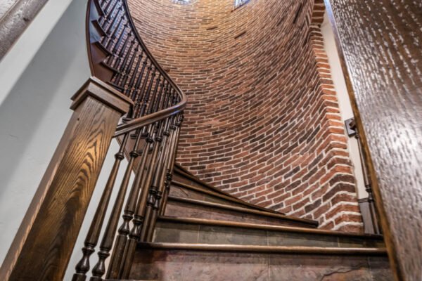 Spiral staircase with wooden railing and exposed brick walls, leading upward in luxury home at 11019 Bridge House Road, Windermere, FL.