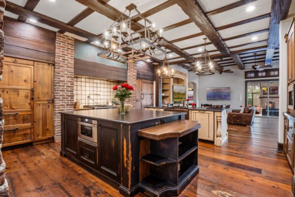 Luxurious kitchen featuring a large island with dark cabinetry, exposed brick walls, wooden beams, and elegant lighting, showcasing the high-end design elements of the estate at 11019 Bridge House Road, Windermere, FL.
