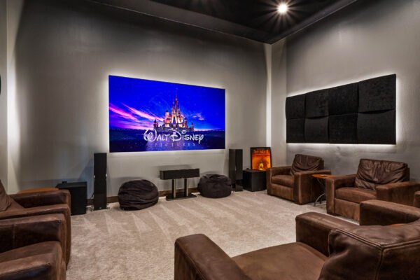 Luxury home theater with plush seating, large screen displaying Walt Disney Pictures logo, and acoustic panels, showcasing entertainment features of the estate at 11019 Bridge House Road in Windermere, FL.