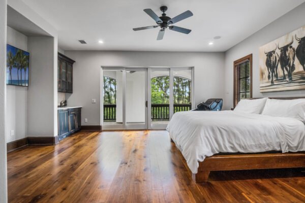 Spacious luxury bedroom with hardwood floors, large windows overlooking nature, king-size bed, and modern decor, showcasing the elegant design of the home at 11019 Bridge House Road in Windermere, FL.