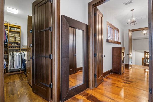 Luxurious interior hallway featuring dark wood doors, a full-length mirror, and warm hardwood flooring, highlighting the elegant design of the master suite in a custom estate at 11019 Bridge House Road, Windermere, FL.