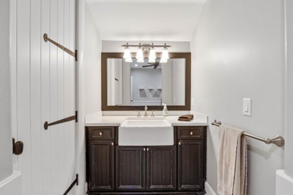 Modern bathroom design featuring a dark wood vanity with a farmhouse sink, stylish light fixtures above a large mirror, and neutral gray walls, highlighting luxury and elegance in the Windermere home.