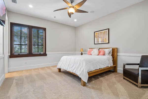Spacious luxury bedroom featuring a wooden bed with white bedding, accent pillows, and a stylish ceiling fan, complemented by large windows and modern decor, showcasing the elegant design of the property at 11019 Bridge House Road in Windermere, FL.