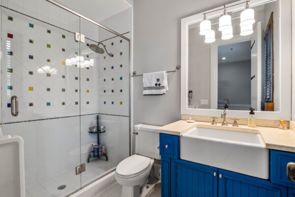 Bathroom featuring a glass shower with colorful tile accents, modern fixtures, blue cabinetry, and a bright mirror, showcasing luxury design in a Windermere home.