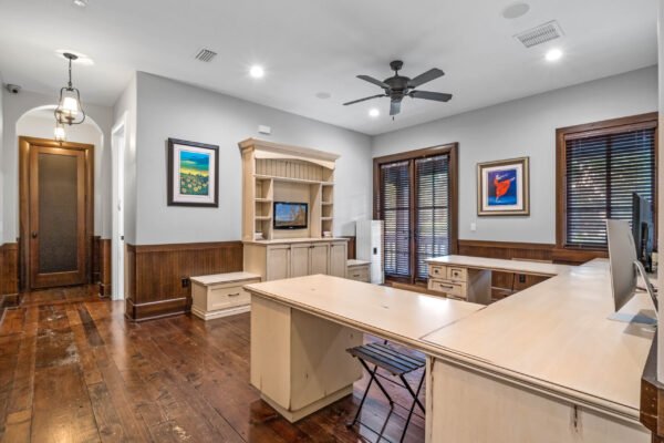 Elegant home office with wooden flooring, custom cabinetry, and dual desks, featuring large windows with blinds and decorative artwork, showcasing a blend of functionality and luxury in a Windermere estate.