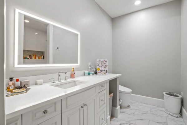 Modern bathroom with a sleek white vanity, illuminated mirror, and marble flooring, showcasing luxury amenities in a custom estate at 11019 Bridge House Road, Windermere, FL.