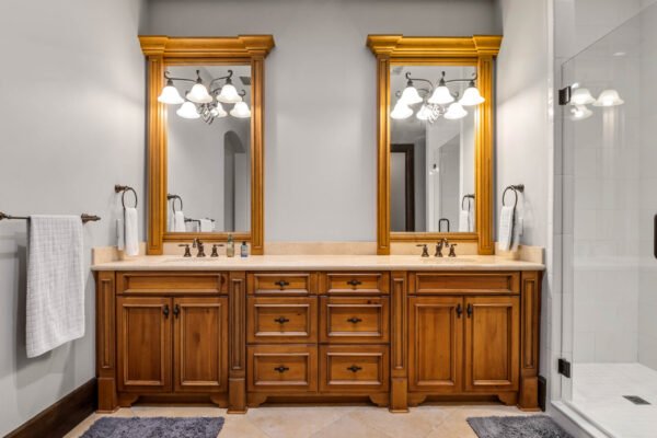 Luxurious bathroom featuring a double vanity with wooden cabinetry, two large mirrors, elegant lighting fixtures, and a glass shower enclosure, showcasing high-end finishes typical of the custom estate at 11019 Bridge House Road in Windermere, FL.