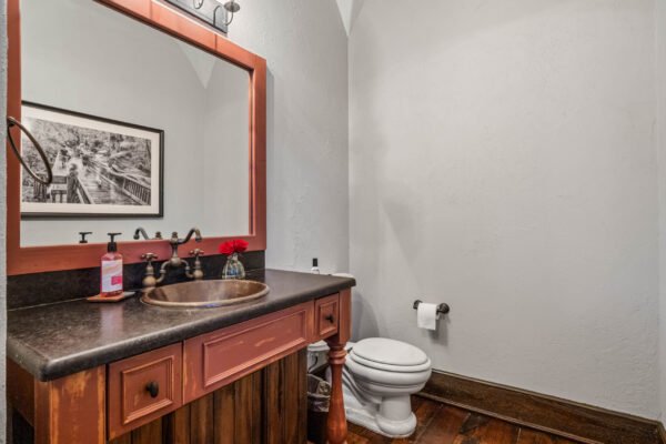 Luxury bathroom with a wooden vanity, bronze sink, and decorative mirror, featuring modern fixtures and a toilet, showcasing elegant design elements in a high-end home.