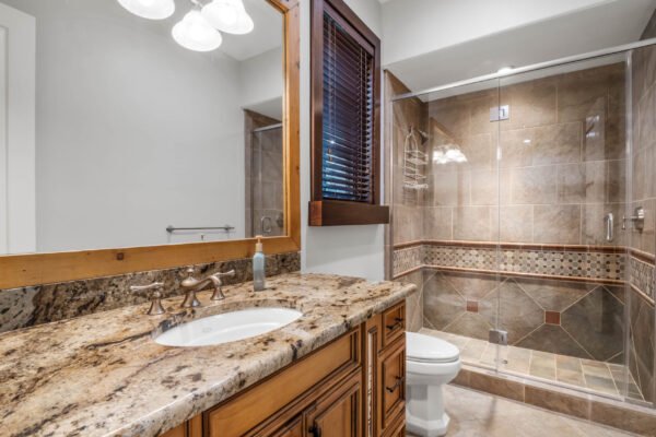 Luxury bathroom featuring a granite countertop, wooden cabinetry, modern fixtures, and a glass-enclosed shower with decorative tile accents, showcasing high-end design elements typical of the custom estate at 11019 Bridge House Road in Windermere, FL.